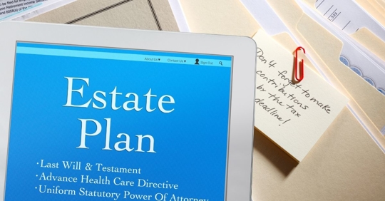 Image of a handheld tablet that reads, "estate plan" on the screen, on top of manila file folders.